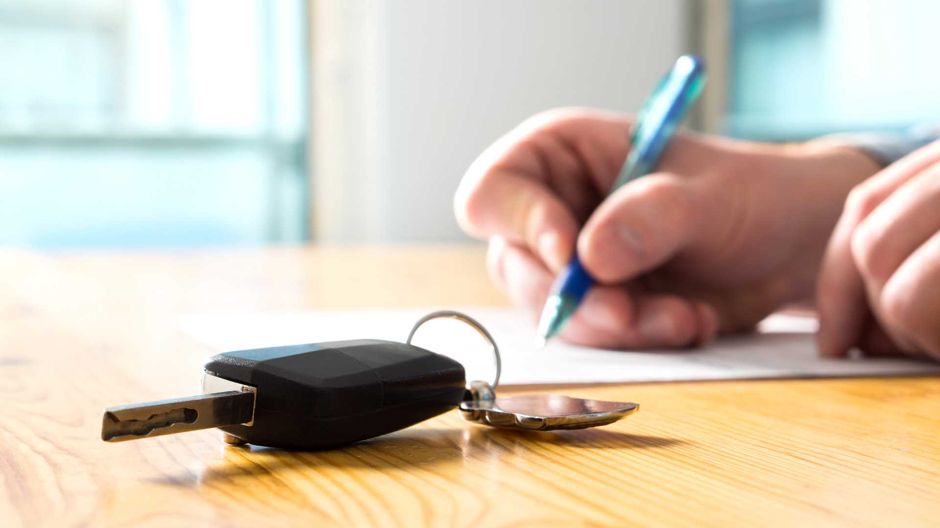 Man signing document with car keys on table